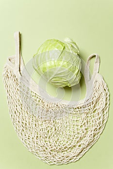 Trendy string bag with fresh young cabbage over light green background