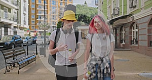 Trendy teenage hipsters boy and girl walking talking on city street, boy with guitar in case