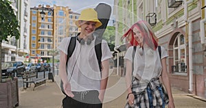 Trendy teenage hipsters boy and girl walking talking on city street, boy with guitar in case