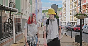 Trendy teenage hipsters boy and girl walking talking on city street, boy with guitar in case