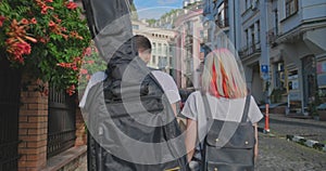 Trendy teenage hipsters boy and girl walking talking on city street, boy with guitar in case, back view