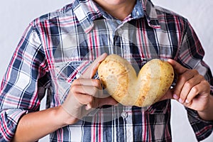 Trendy ugly vegetable heart shaped potato in hands