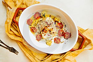 Trendy vegan health food. feta cheese with small tomatoes in olive oil with herbs and spices in a ceramic orange baking dish.