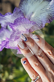 Trendy wavy manicure nails on iris flower background. Summer mood, nail art.