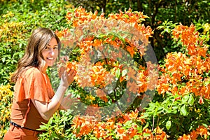 Trendy woman admiring colorful orange azaleas in spring