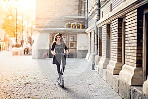 Trendy woman, beautiful brunette girl riding electric scooter in city