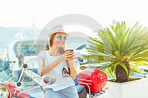 Trendy woman drinking takeaway coffee near her red moped on the