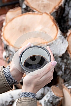 Trendy woman holding a metal mug at a picnic. White travel cup with coffee. Vertical shot