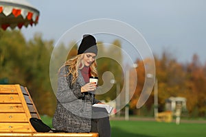 Trendy woman in stylish coat sitting on the bench in city park. Urban scene outdoors.