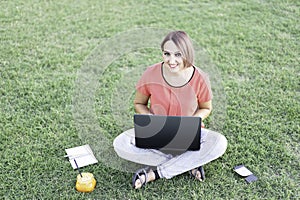 Trendy woman working outdoors with laptop - Smiling woman sitting on lawn typing on pc - Orange juice is ready for break - Healthy