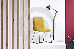 Trendy yellow chair on platform and tall black industrial lamp behind it in white and bright interior with purple and wooden walls