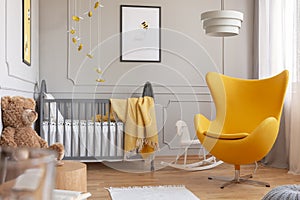 Trendy yellow egg chair in elegant grey nursery with wooden crib and posters on the wall