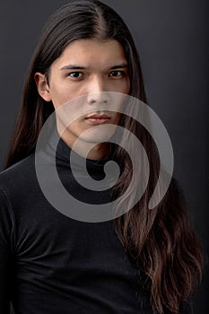 Trendy young man dressed in black shirt posing in modern studio against dark wall