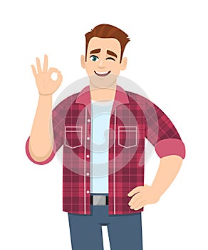 Trendy young man showing okay sign and winking eye. Stylish person making OK or cool gesture with fingers. Male character.