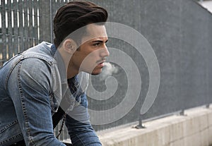 Trendy young man sitting outside smoking