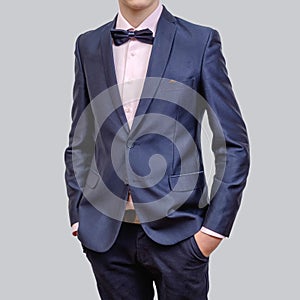 Trendy young man wearing blue blazer and tie bow, standing against a grey background