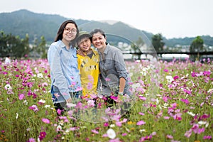 Trendy young mother and her two teenagers kids happily posing by field of flowers.