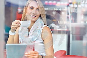 Trendy young woman in cafe with cup of coffee and touchscreen tablet