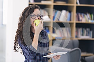 Trendy young woman eating a green apple. Over library background