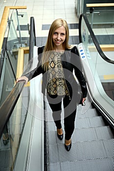 A trendy young woman going up to a business building with an escalator in the business district of London, England