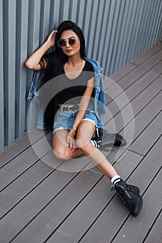 Trendy young woman hipster with long hair in fashionable jeans clothes in stylish black leather boots sits in the city