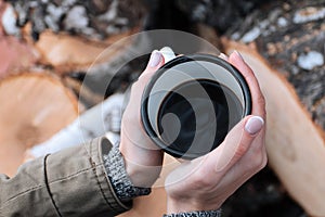 Trendy young woman holding a metal mug at a picnic. White travel cup with coffee