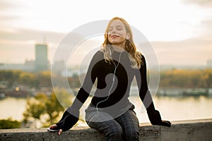 Trendy young woman listening music from smartphone outdoor at sunset