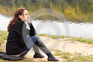 Trendy young woman sitting on a river bank