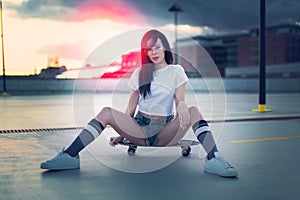 Trendy young woman sitting on skateboard in sunset