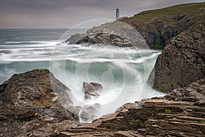 Trevose Head Lighthouse in North Cornwall with a stormy sky and waves crashing on the rocks makes a beautiful rugged landscape