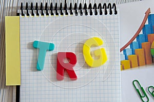 TRG - an abbreviation in multi-colored letters lies on a notebook against the background of a graph