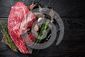 Tri Tip black angus beef steak on cutting board with herbs, raw meat. Black Wooden background. Top view. Copy space