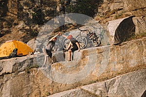 trial bikers resting and giving high five to each other near tent and mountain cycles on rocky