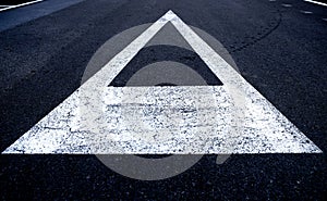 A triangle arrow direction marked in a white painted sign on a black asphalt road.