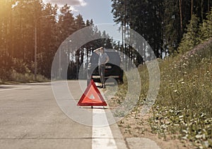 Triangle caution sign on road side after car break down and sad female driver waiting for emergency repair service