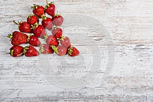 A triangle of fresh ripe red strawberries lies on a light textured wooden table
