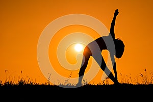 Triangle pose yoga with young woman silhouetted.