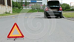 Triangle warning sign on road foreground and car with blinker lights on road wayside
