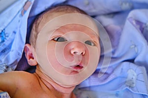 Triangular alien - shaped face of a newborn baby, a portrait with the emotion of surprise in a child