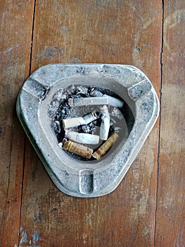 a triangular cigarette ashtray containing cigarette butts on a wooden plank background