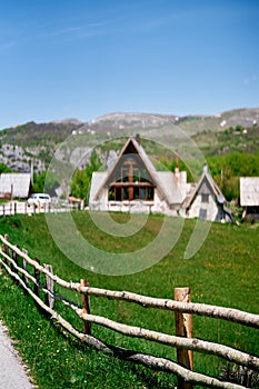 Triangular houses in a green valley behind a wooden fence along the road at the foot of the mountains