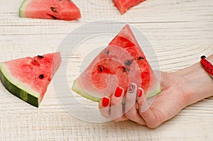 Triangular piece of watermelon in a female hand with a manicure on a light wooden background