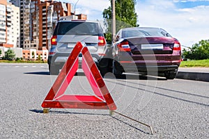 Triangular red retro-reflective sign of accident on the road. Collision of two cars. Broken bumper and hood. Car