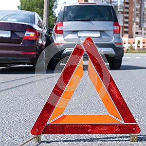 Triangular red retro-reflective sign of accident on the road. Collision of two cars. Broken bumper and hood. Car