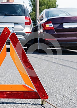 Triangular red retro-reflective sign of accident on the road. Collision of two cars. Broken bumper and hood. Car accident on the