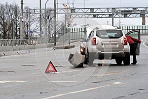 Triangular red retro-reflective sign of accident on the road. Collision of two cars. Broken bumper and hood. Car accident on the