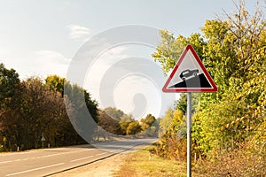 Triangular road sign steep climb against the background of autumn trees near the track