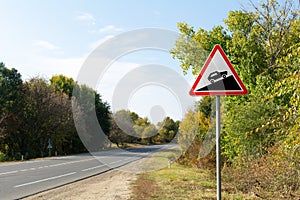 Triangular road sign steep climb against the background of autumn trees near the track