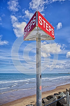 Triangular sign to mark where steps are on a beach. West Cliff beach, Whitby, North Yorkshire.