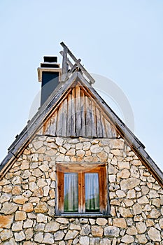 Triangular stone house with a wooden roof and a chimney against a blue sky